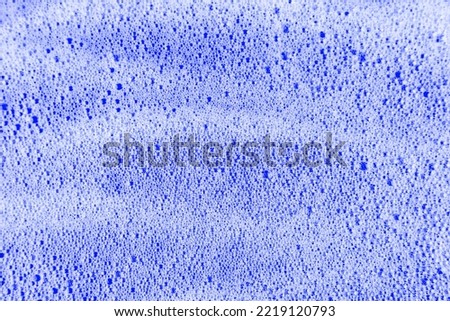 White cosmetics foam texture on blue backdrop. Cleanser, soap, shampoo bubbles. Foamy skin care product sample. Skincare, cosmetology and beauty concept