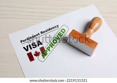 Document with approved permanent residency visa in Canada and stamp on white wooden table Royalty-Free Stock Photo #2219131321