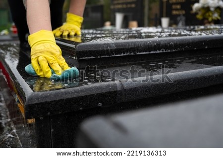 Headstone cleaning on cemetery. Professional in yellow gloves cleans the marble grave, scrubbing with sponge and water. Tombstone preparation for All Saints Day on November 1st Royalty-Free Stock Photo #2219136313