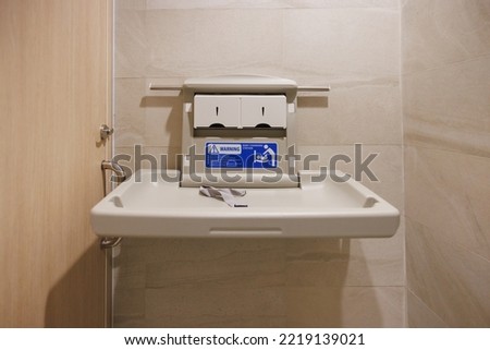 white plastic diaper table on marble tile wall in toilet. Baby changing station in a public restroom.