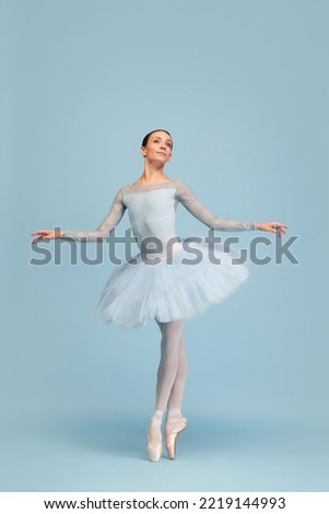 Portrait of tender young ballerina dancing, performing isolated over blue studio background. Beauty of classical dance. Concept of classic ballet, inspiration, beauty, dance, creativity