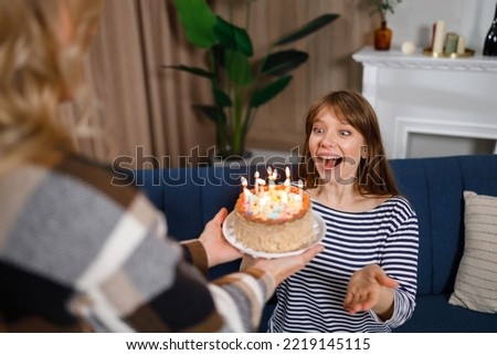 Happy birthday my sweetie. Woman gives a cake with candles to her daughter who sitting on the sofa