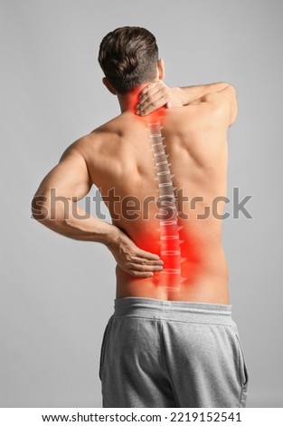 Man suffering from back and neck pain on light grey background Royalty-Free Stock Photo #2219152541