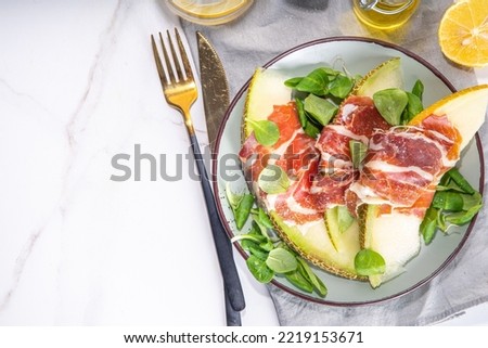Fresh melon salad with prosciutto hamon and green leaves mix, autumn fruit vegetable salad, portion on plate, on white marble background copy space