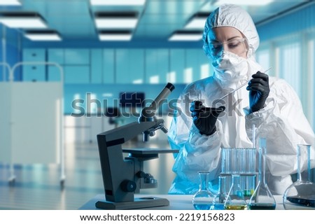 Virologist is working. Woman virologist in chemical protection suit. Girl is studying dangerous viruses. Biologist at laboratory table. Virological clinic employee. Virologist works with microscope Royalty-Free Stock Photo #2219156823