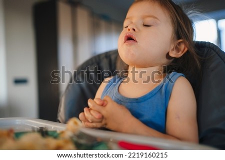 Caucasian baby girl sitting in the high-chair with her mouth open and her eyes closed, her stomach full after a rich meal. Healthy eating. Child health care