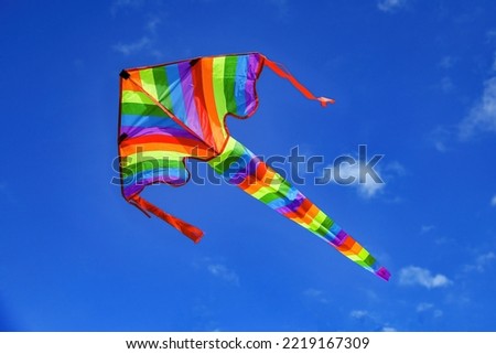 A colorful kite soars among the blue cloudy sky.