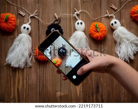 The hand with the phone takes pictures of the background with ghosts, pumpkins and other elements. Halloween. Content for various purposes
