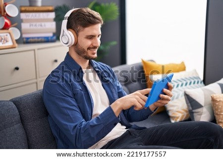 Young caucasian man watching video on touchpad sitting on sofa at home