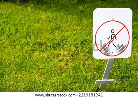 Close up of metal sign with red crossed out figure placed on lawn in public park on green area as concept of prohibition of entering green parks public areas