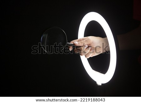 Female hand holding magnifying glass through led ring lamp on black background. Business concept