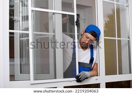 Professional installation of mosquito nets on a plastic window using external plastic or metal fasteners. Worker carefully installs the insect repellent grid on open window Royalty-Free Stock Photo #2219204063