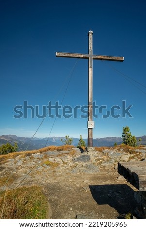 Wooden cross on the top of Gerlosstein in Austrian Alps with mountain panorama in the back on a sunny day of autumn with blue sky above. Mountain top on a sunny day.