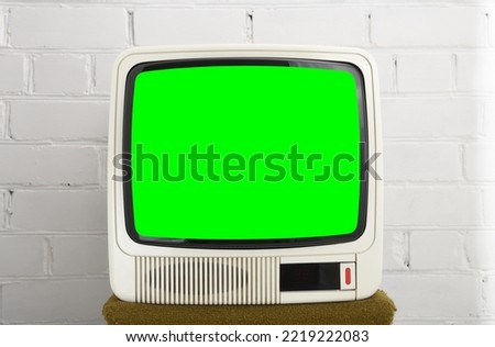 An old white TV from the 90s with a green screen against a brick wall. Retro technology concept.