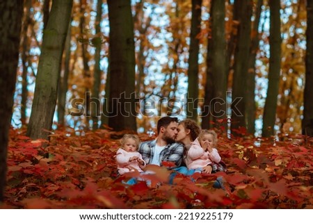 a family is walking in the middle of autumn nature with two little twin sisters; 
parents with children sit in the middle of a colorful forest on a warm autumn day