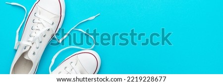 Flat lay top-down composition of pair of white untied sneakers. Minamalist flat lay image of white gumshoes over turquoise blue background with copy space.