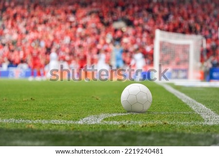 White ball at the corner of soccer pitch with players and fans in background.