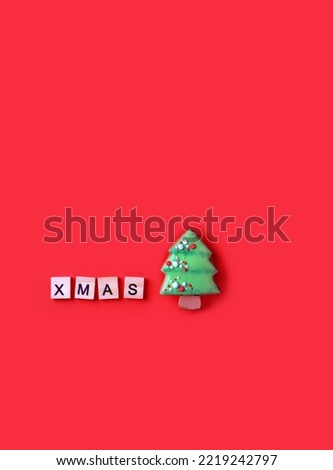 gingerbread Christmas tree shaped cookie and wooden letters "xmas" on red background close up. symbol of Christmas holiday, Advent. Festive winter season. minimal style. top view