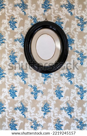 Vintage blank oval picture frame hanging on a wallpaper decorated wall