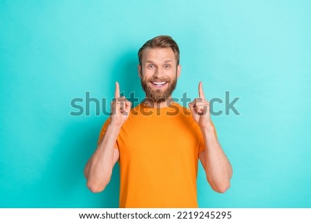 Portrait of impressed handsome astonished guy blond beard wear orange t-shirt indicating empty space isolated on teal color background