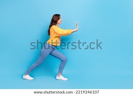Full length photo of funny pretty girl dressed yellow pullover pulling huge empty space isolated blue color background