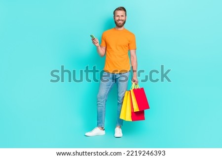 Full size photo of masculine beard guy hold telephone bags wear t-shirt jeans sneakers isolated on teal color backgroiund