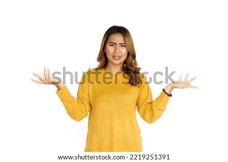 Attractive positive young asian brunette woman in yellow sweater on white background, palm up and surprise