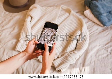 Close-up of woman's hands taking picture of her used sweater. Selling used clothes online, reuse, sustainable consumption