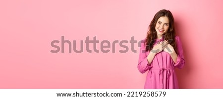 Image of beautiful young woman holding hands on heart and smiling grateful, express gratitude, saying thank you, receive heartwarming gift, standing over pink background.