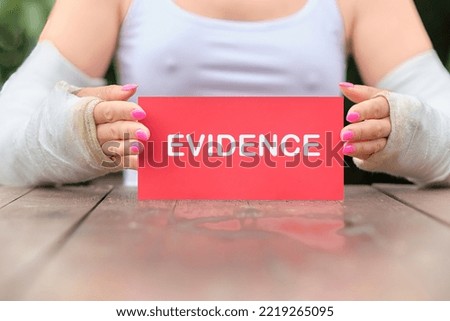 Women's hands in casts because of a broken arm are carefully holding a red card with the word Evidence, a business concept.