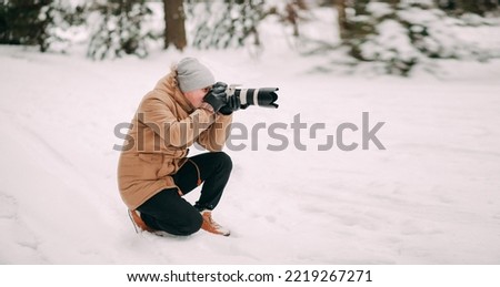 Man with camera in winter forest. Photographer takes pictures or shooting video of trees under snow, scenery. Nature photographer tourist with camera shoots. Leisure activity in cold season