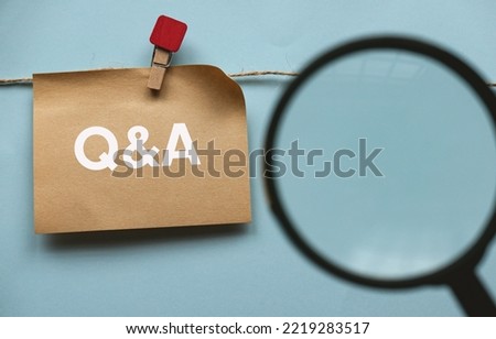 Brown paper hanging on the rope written with letter Q, A and ampersand with a blurry image of magnifying glass in front. Question and answer concept.