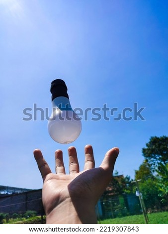 Human hand with floating white bulb with clear blue sky in the morning. Conceptual Illustration for growing business, Creative, ideas, and green energy.
