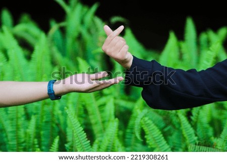 Close-up view of young couple in love made a korean love sign with blurred green leaves background in a park.