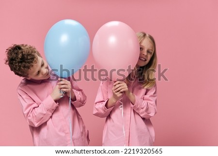 school-age children stand holding balloons in their hands and look out from behind them smiling. Horizontal photo on an empty pink background with space for inserting advertising text