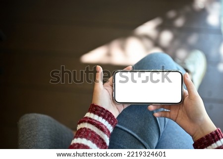 A female watching some video on her smartphone while relaxing in the coffee shop. A female holding a mobile phone white screen mockup in a horizontal position.