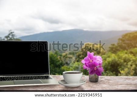 A white coffee mug and laptop is placed on old wooden top table with blurred nature background. Good morning or have a happy day . image