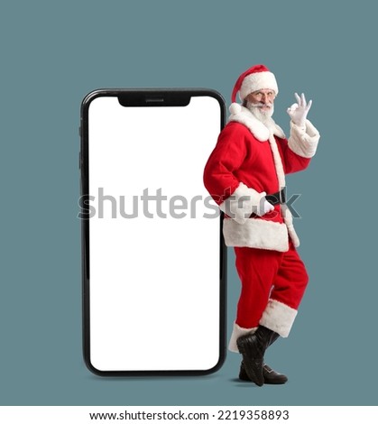 Santa Claus showing OK and big smartphone on grey background Royalty-Free Stock Photo #2219358893