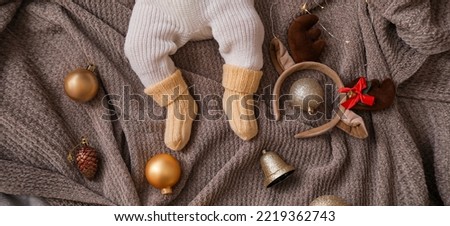 Legs of cute little baby with Christmas decor lying on plaid, top view
