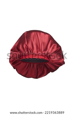 Close-up shot of a red sleep cap with a wide elastic band. A satin hair bonnet for protecting hair at night is isolated on a white background. Front view. Royalty-Free Stock Photo #2219363889