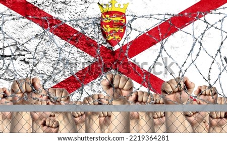 Raised fists against the background of the depicted flag of Jersey behind barbed wire.