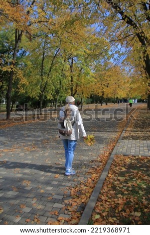 The photo was taken in the city of Odessa. The picture shows a young woman walking in a public autumn park with bunches of yellow leaves in her hand. 