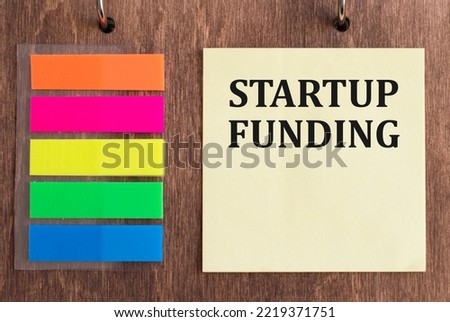 funding a startup text on a yellow card on a wooden background next to colored stickers