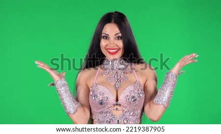 Portrait of beautiful woman in a chic dress for oriental dances looking straight with shocked and surprised wow face expression. A brunette with long hair, bright eyes and red lips on green screen.