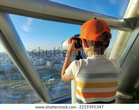 Toddler boy looking through large binocular shape. a boy looks through a telescope at the city. Traveling with children. Interesting trip with students.
