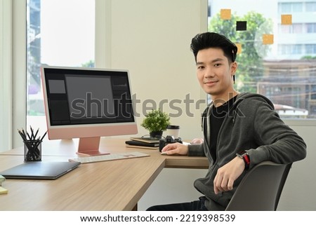 Handsome male photo editors sitting in creative workplace front of personal computer and smiling to camera