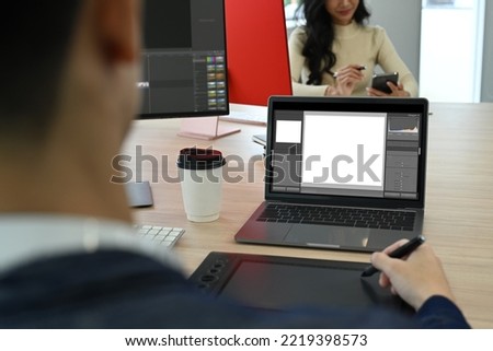 Over shoulder view of male photo editors sitting in creative workplace and retouching photos on laptop computer