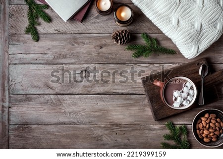 Hot coffee drink, almonds, cosy knitted sweater on wooden background with candles and pine cones, copy space. Hygge and home comfort concept. Seasonal winter cosy composition.