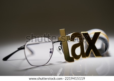 single word tax eyeglasses and roll of us currency                            Royalty-Free Stock Photo #2219415119