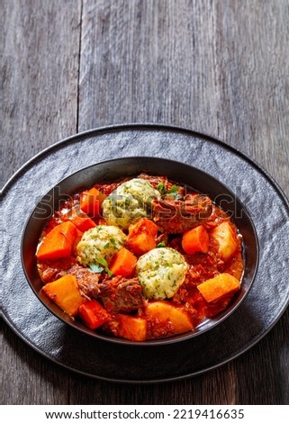 Beef Stew with Dumplings and vegetables in rich tomato and stock based gravy in black bowl, british cuisine, vertical view from above, free space